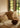 A cottage-style living room filled with earthy palette handwoven pillows and antique objects. It is furnished with a white sofa and twin armchairs in front of a fireplace.