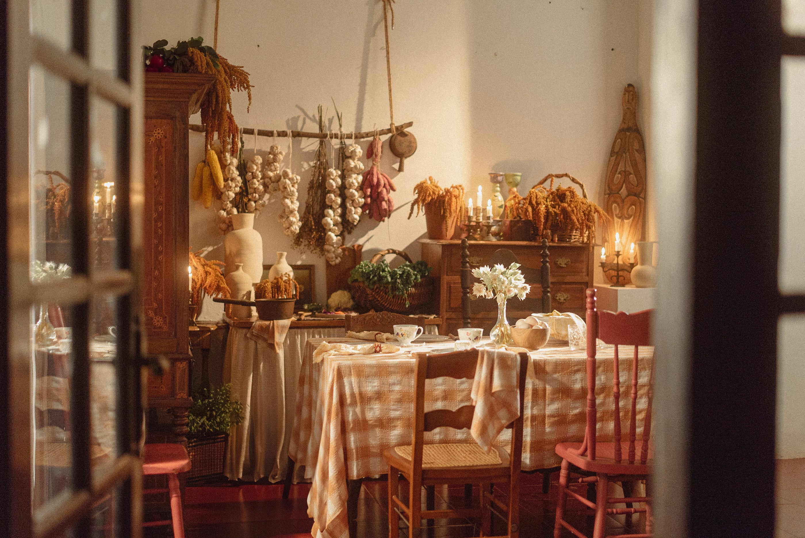 Vintage kitchen ambiance featuring dried flowers adorning the walls, complemented by a dining table adorned with a pink checkerboard tablecloth.	
